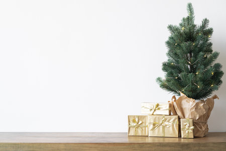 a small Christmas tree with warm bulbs in a pot on a wooden table with gifts wrapped in gold paper. the concept of Christmas. High quality photoの写真素材