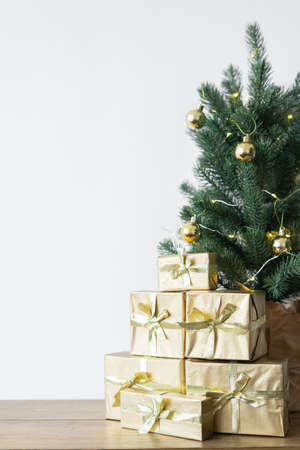 a small Christmas tree with warm bulbs in a pot on a wooden table with gifts wrapped in gold paper. the concept of Christmas. High quality photoの写真素材