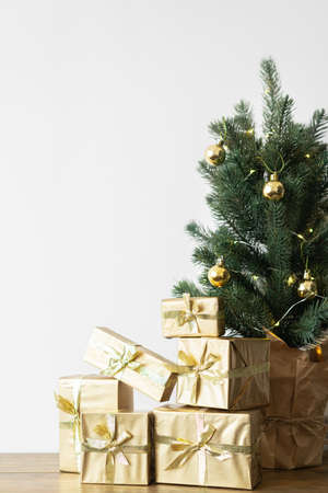 a small Christmas tree with warm bulbs in a pot on a wooden table with gifts wrapped in gold paper. the concept of Christmas. High quality photoの写真素材