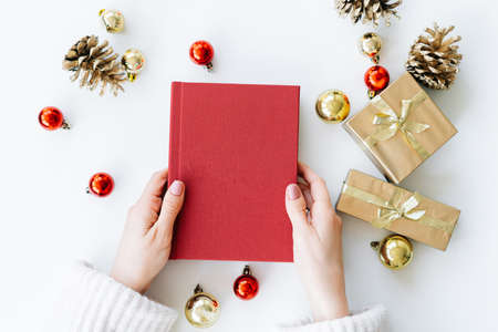 a red book in the hands of a young girl against the background of gifts and Christmas toys. the concept of Christmas. High quality photoの写真素材