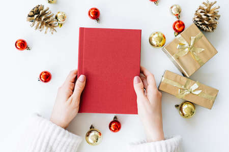 a red book in the hands of a young girl against the background of gifts and Christmas toys. the concept of Christmas. High quality photoの写真素材