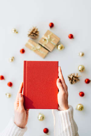 a red book in the hands of a young girl against the background of gifts and Christmas toys. the concept of Christmas. High quality photoの写真素材