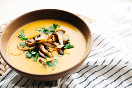 a plate of hot homemade pumpkin-coconut cream soup with fried mushrooms and fresh herbs. High quality photoの写真素材