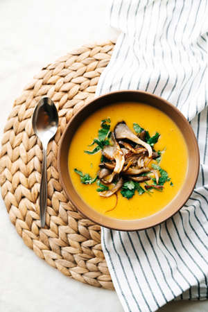 a plate of hot homemade pumpkin-coconut cream soup with fried mushrooms and fresh herbs. High quality photoの写真素材