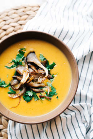a plate of hot homemade pumpkin-coconut cream soup with fried mushrooms and fresh herbs. High quality photoの写真素材