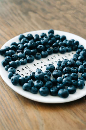 a white plate with a motivational phrase and fresh ripe blueberries on a wooden tableの写真素材