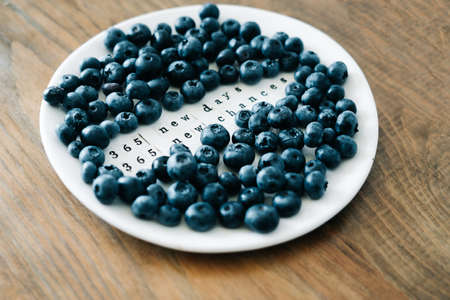 a white plate with a motivational phrase and fresh ripe blueberries on a wooden tableの写真素材