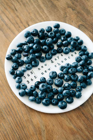 a white plate with a motivational phrase and fresh ripe blueberries on a wooden tableの写真素材