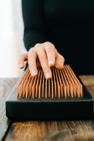 a sadhu board made of dark oak with copper nails on a wooden table. the girl runs her fingers over the copper nails. the yogic practice of standing on nailsの写真素材