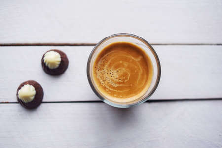 Two chocolates candies and cup of espresso on the white wooden table. Top view. Place for text.の写真素材