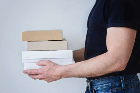 A strong man in jeans and black t-shirt is holding three boxes in his hands.