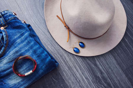 Gray elegance hat with blue earrings and blue jeans outfit on the wooden background.の写真素材