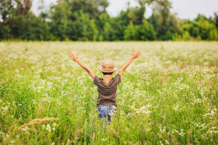 Adorable kid boy in straw hat standing on a summer meadow. Sunset in the park. Outdoors. Vacations. Walking in the farm.の写真素材