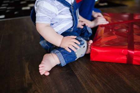 Body part, children fingers feet on the wooden brown floor near the red present. Cozy home location.の写真素材