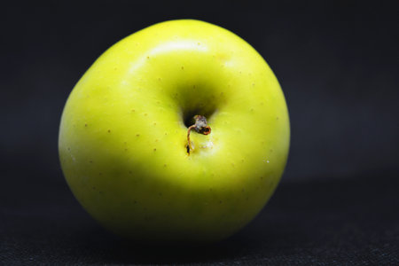 Ripe juicy green apple, fresh fruit is located on a black fabric background.