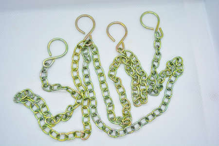 Metal chains, overflow chains and large hooks are arranged randomly on a white fabric background.