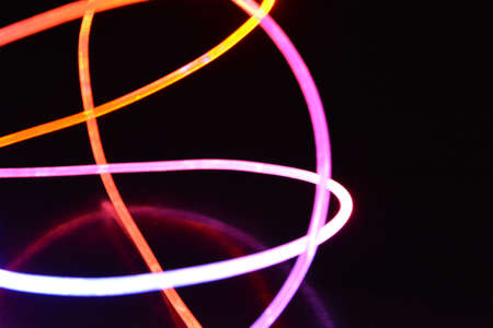 Yellow and blue light wire, a light guide wire with different light transmission, light spectrum, and light effects located in a chaotic state with light reflection on a black glossy background.の写真素材