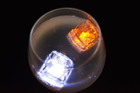 White and yellow bright glowing ice cubes that float in a delicious frosted white cold drink are located in a cognac glass on a black frosted background.の写真素材