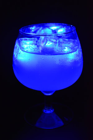 Blue bright glowing ice cubes that float in a delicious frosted white cold drink are located in a cognac glass on a black frosted background.の写真素材