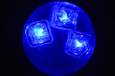 Blue bright glowing ice cubes that float in a delicious frosted white cold drink are located in a cognac glass on a black frosted background.の写真素材