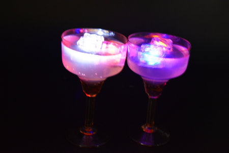 Two yellow deep champagne glasses with a white drink, diode lights and luminous ice cubes are located on a black matte background.の写真素材