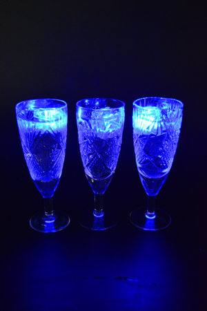 Crystal champagne glasses with carvings in the form of snowflakes are located on a black matte background. Bright multicolor doidic glowing ice cubes float in the drink.の写真素材