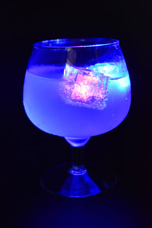 Blue and yellow bright glowing ice cubes that float in a delicious frosted white cold drink are located in a cognac glass on a black frosted background.の写真素材
