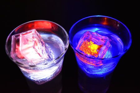 A champagne glass with a pattern of branches and leaves filled with a white drink is located on a black matte background. Small ice cubes glowing in different colors float in a glass, party, celebratiの写真素材
