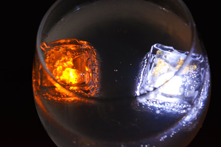 White and yellow bright glowing ice cubes that float in a delicious frosted white cold drink are located in a cognac glass on a black frosted background.の写真素材