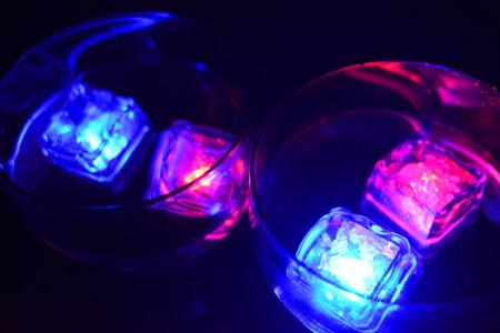 Large glasses with different colors of luminous ice cubes with a tasty drink are located on a black matte background.の写真素材