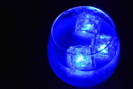 Blue bright glowing ice cubes that float in a delicious frosted white cold drink are located in a cognac glass on a black frosted background.の写真素材
