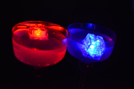 Two yellow deep champagne glasses with a white drink, diode lights and luminous ice cubes are located on a black matte background.の写真素材
