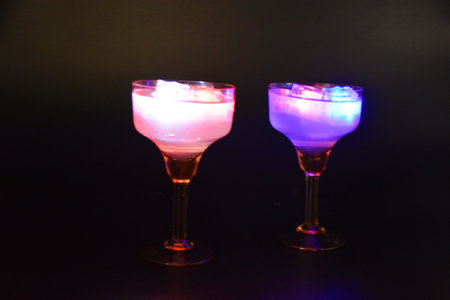 Two yellow deep champagne glasses with a white drink, diode lights and luminous ice cubes are located on a black matte background.の写真素材