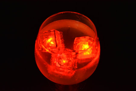 Red bright glowing ice cubes that float in a delicious frosted white cold drink are located in a cognac glass on a black frosted background.の写真素材
