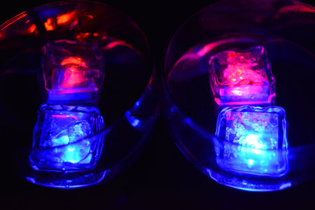 Large glasses with different colors of luminous ice cubes with a tasty drink are located on a black matte background.の写真素材