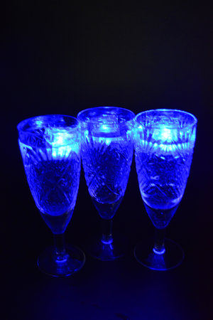 Crystal champagne glasses with carvings in the form of snowflakes are located on a black matte background. Bright multicolor doidic glowing ice cubes float in the drink.の写真素材