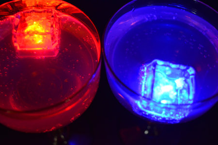 Two yellow deep champagne glasses with a white drink, diode lights and luminous ice cubes are located on a black matte background.の写真素材