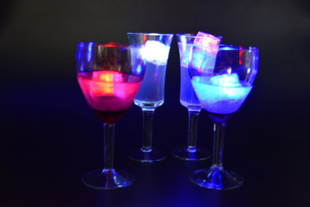 Four glasses with bright different colors of luminous led ice cubes are located on a black background.の写真素材