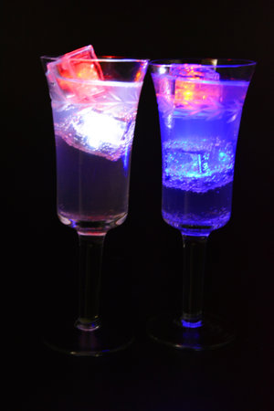 A champagne glass with a pattern of branches and leaves filled with a white drink is located on a black matte background. Small ice cubes glowing in different colors float in a glass, party, celebratiの写真素材