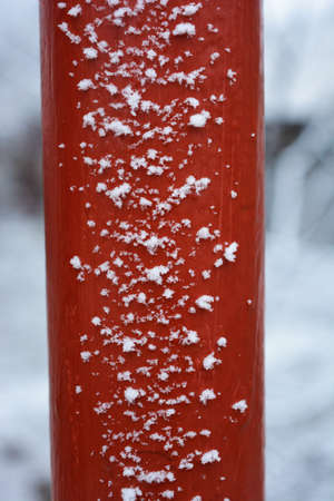 Red metal pipe covered with large and fluffy snowflakes during a snowfall in winter.の写真素材