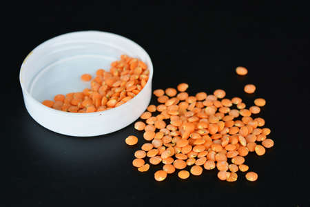 Grains, seeds of red lentils, a handful of lentils are located and scattered in a white plastic...