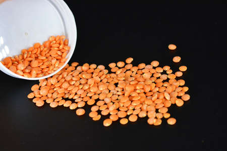Grains, seeds of red lentils, a handful of lentils are located and scattered in a white plastic...
