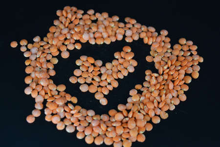 Grains, seeds of red lentils, a handful of lentils are located and scattered on a black plastic background.の写真素材