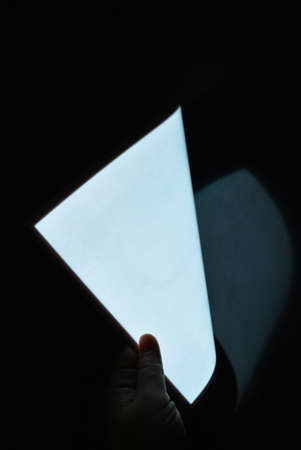 Very bright and luminous A4 electroluminescent paper with an coating is located in different flatnesses on a pristine glossy surface with a female hand. Excellent color substrate, uniform glow.の写真素材