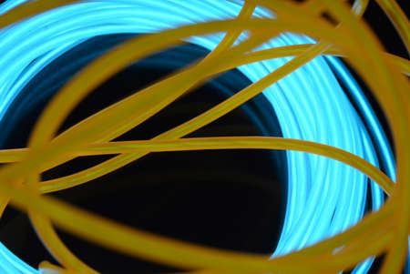 A bright coil of turquoise, sky blue luminous wire with chaotic wires of an orange light guide...