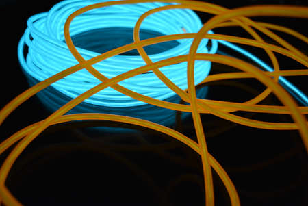 A bright coil of turquoise, sky blue luminous wire with chaotic wires of an orange light guide...