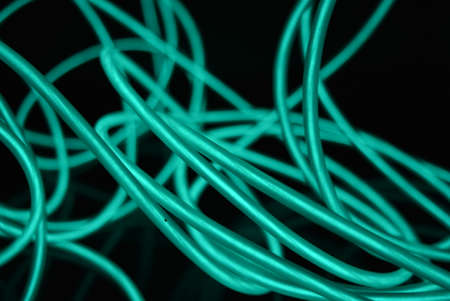 Unusual bright wires made of turquoise-colored material glowing at night. Chaotic sky blue wires, light guide electroluminescent wires, electroluminescence are located on a glossy black surface.の写真素材