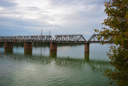 The gray Samara railway bridge over the surface of the Samara river with a beautiful landscape, green trees, bushes and greenery. Pictures of the river landscape with an unusual sky and bright clouds.の写真素材
