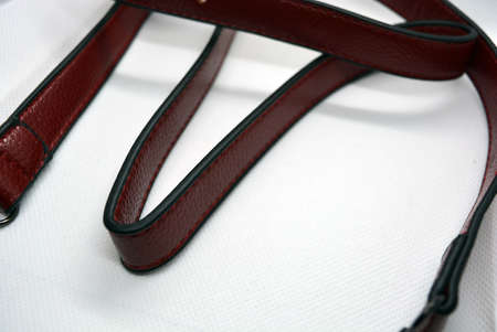 Red leather belt with metal buckle. Leather accessory ribbon chaotically scattered on a white...