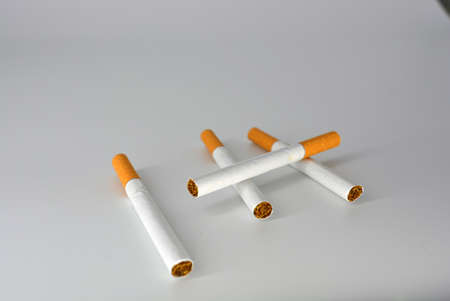 Many white cigarettes with a brown filter chaotic arranged on a white background. Smoking is...